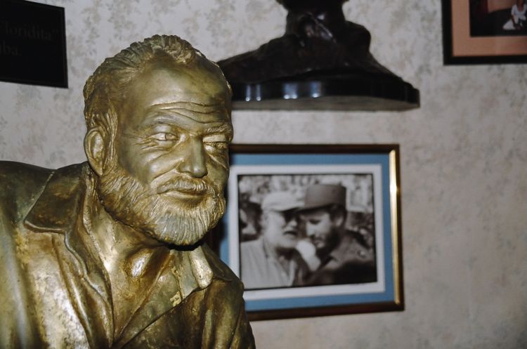 Ernest Hemingway's statue at his favorite Daquiri place - El Floridita in Havana; in the back: photo of Hemingway & young Fidel Castro